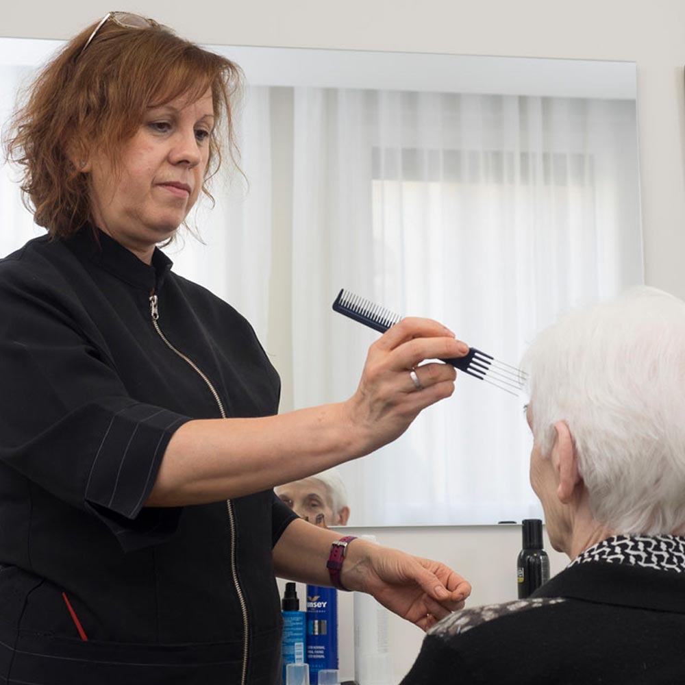 La peluquera del centro de mayores peinando a una residente